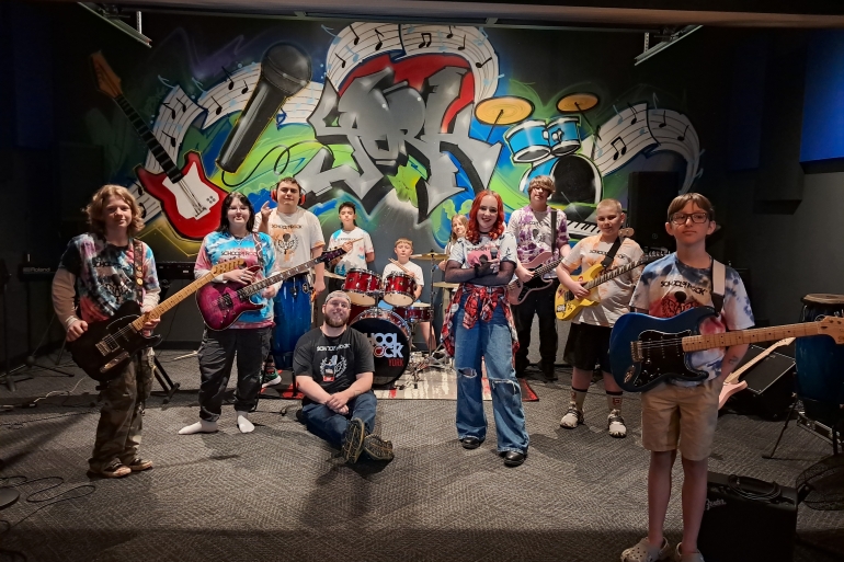 Students from School of Rock York 2025 Summer Camp season pose with their instruments and teacher