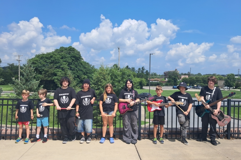 Students from School of Rock York 2025 Summer Camp season pose outside with their instruments