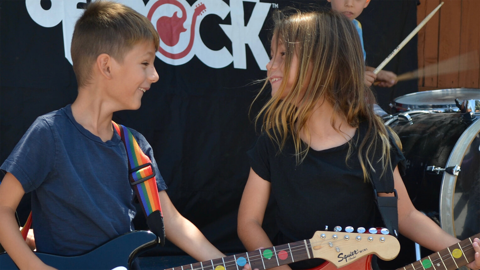 summer camp, guitar lessons, bass lessons, no experience needed, drum lessons, guitarists looking at each other, rock out on stage, kid playing guitar