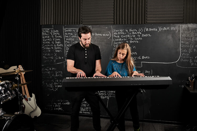 A School of Rock instructor teaches a child to play the keyboard