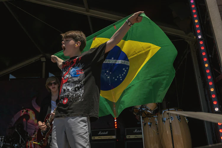 Aluno da School of Rock Ribeirão Preto no palco do Rock in Rio Lisboa, segurando a bandeira do Brasil