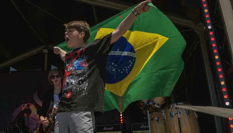 Aluno da School of Rock Ribeirão Preto no palco do Rock in Rio Lisboa, segurando a bandeira do Brasil