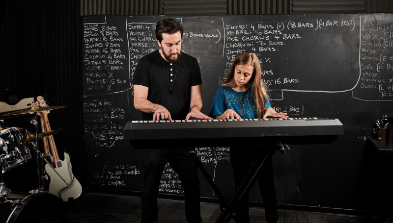A School of Rock instructor teaches a child to play the keyboard