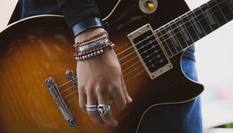 A closeup of a student playing a les paul, wearing bracelets and rings on their strumming hand