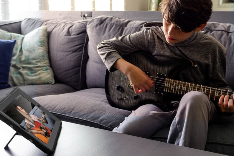 Garoto em casa utilizando um Ipad durante sua aula de guitarra
